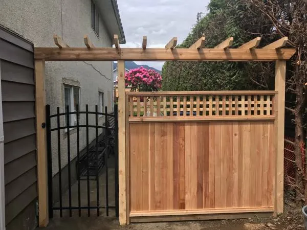 Cedar gate with a lattice top under a cedar arbour, beside a black metal gate