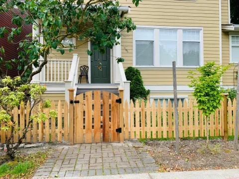 Cedar picket fence with a matching gate in front of a yellow house