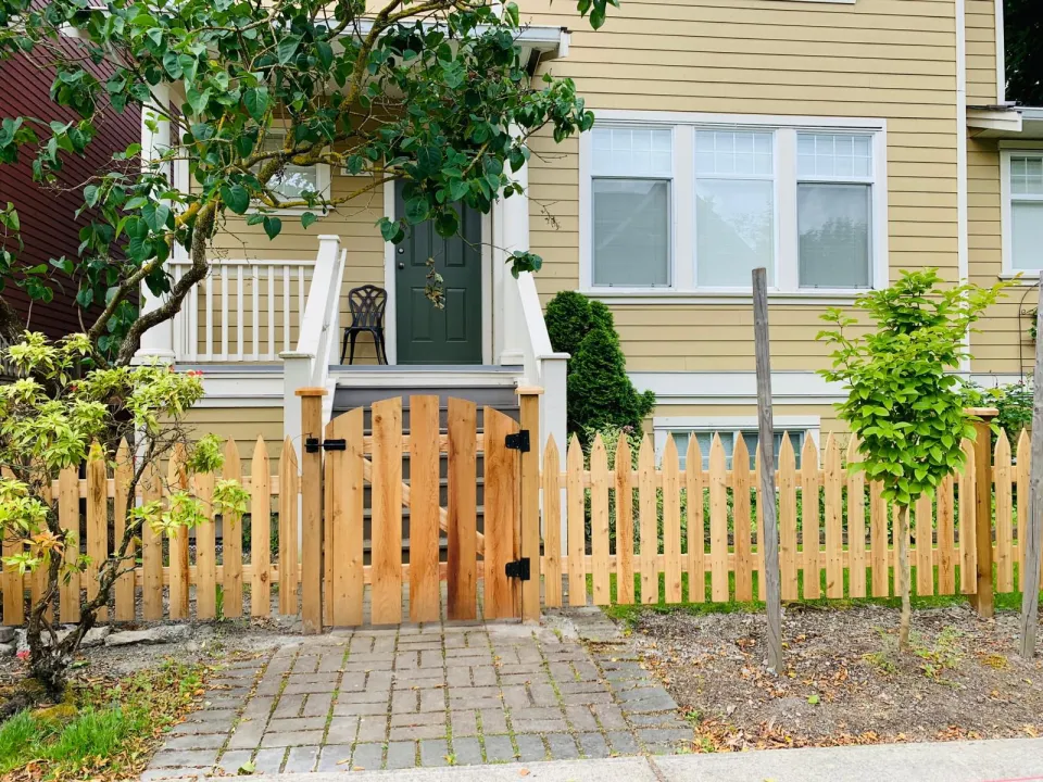 Cedar picket fence with a matching gate in front of a yellow house