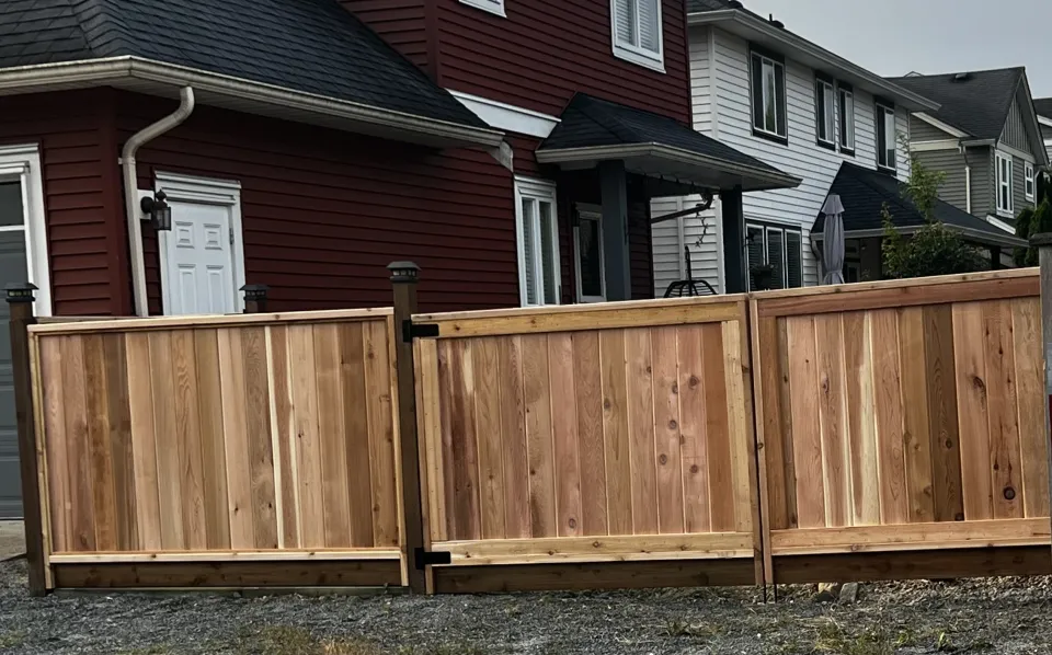 Framed cedar privacy fence with a top cap in front of a red house