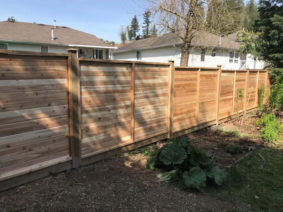 Horizontal cedar privacy fence with framed panels and post caps along a backyard garden