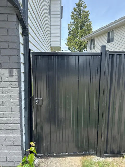 Black steel single gate between a house and fence