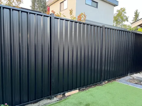 Black steel privacy fence with matching posts along a lawn