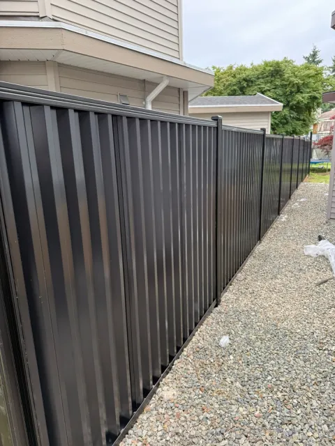 Black steel privacy fence down a gravel side yard