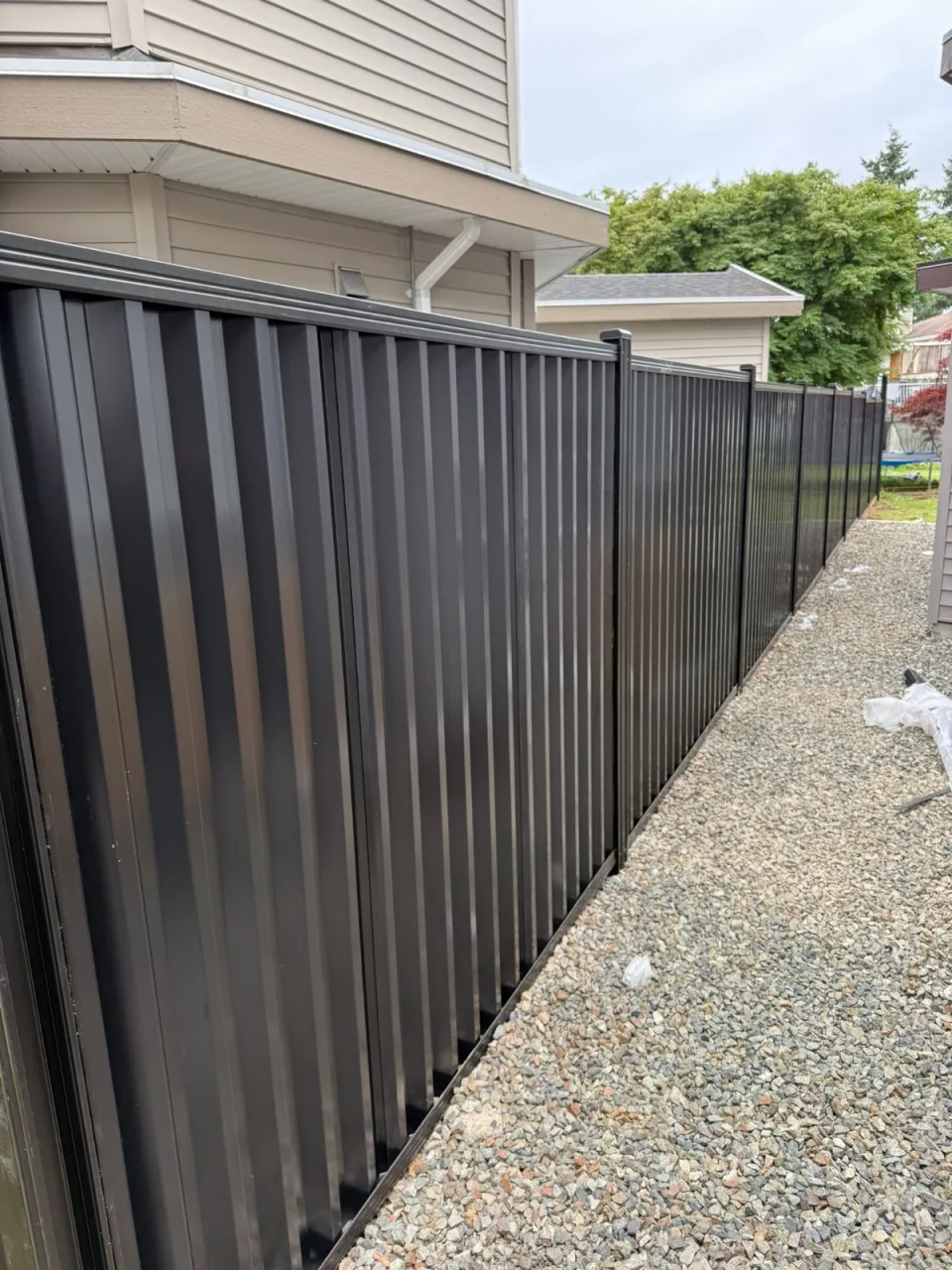 Black steel privacy fence down a gravel side yard