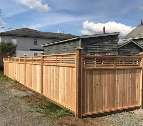 Cedar fence with a slat top and a gate beside a gravel area