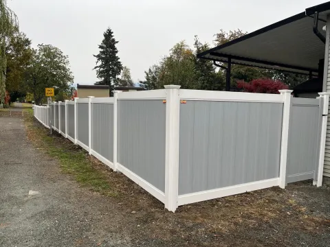 Grey vinyl fence with white posts along a gravel lane